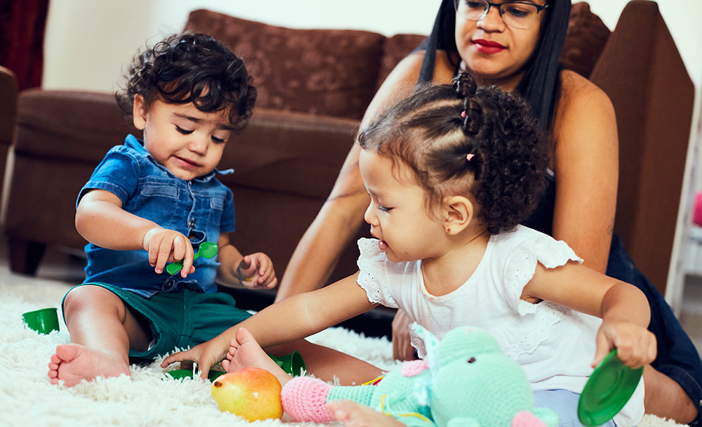 Mãe sentada no chão da sala brincando com os filhos